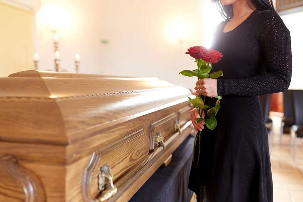 A small group of people gathered outdoors around a wooden casket during a traditional funeral ceremony.
