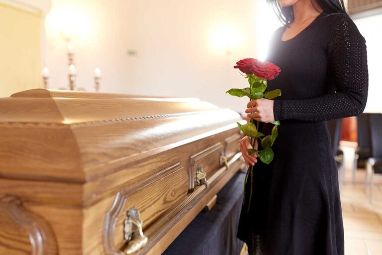 A small group of people gathered outdoors around a wooden casket during a traditional funeral ceremony.